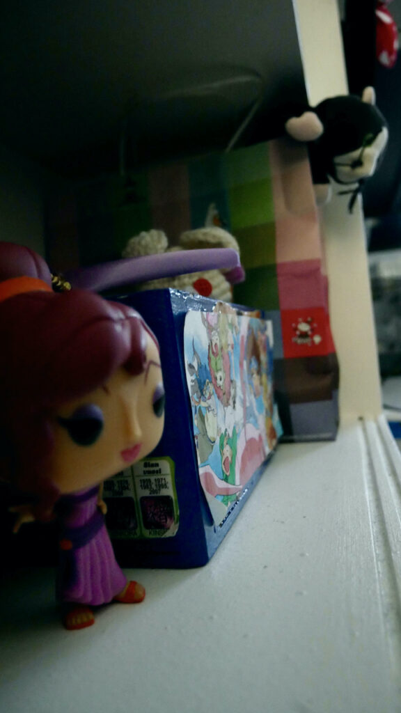 around blue woodenbox there's Megara funko pop figurine and cat doll inside a paper bag