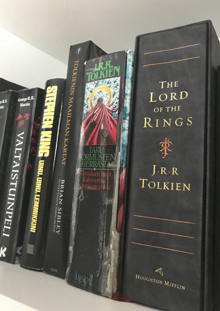 Kuvassa useampi mustaselkäinen kirja kirjahyllyssä. Kirjat vasemmalta oikealle: The Lord of the Rings, Taru sormusten herrasta, Tolkienin maailman kartat, Uinu, uinu, lemmikkini, Valtaistuinpeli.