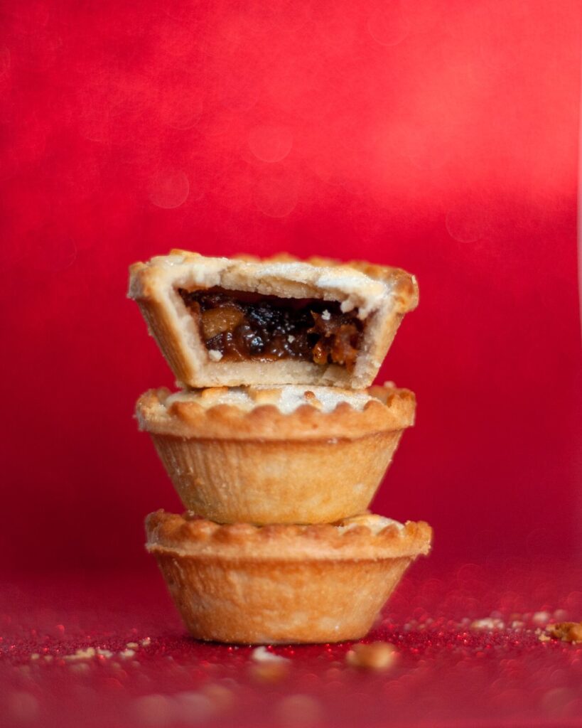 Kuvassa on punaista taustaa vasten pinossa kolme mince pies -leivosta.