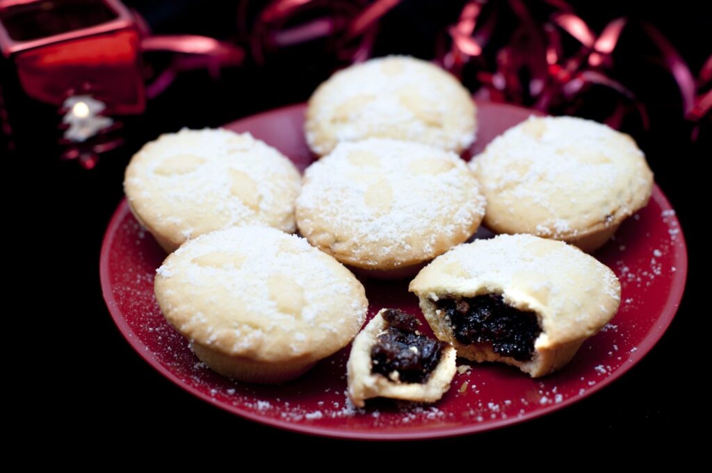 Kuvassa on punaisella lautasella mince pies -leivoksia.